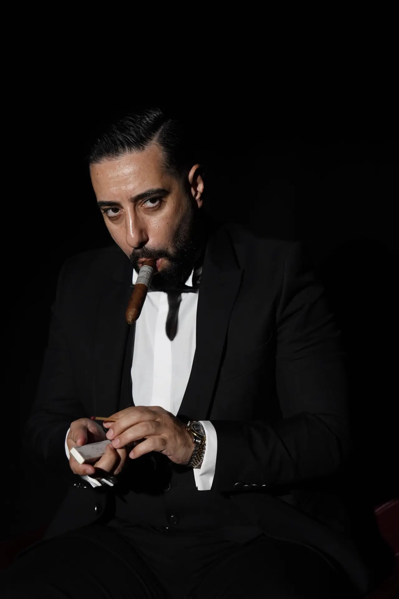 Siyah smokinle, puro ağzında, kameraya yoğun bir bakış